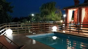 Piscina con cubierta de madera y sillas de descanso, rodeada por una cerca de madera y árboles.