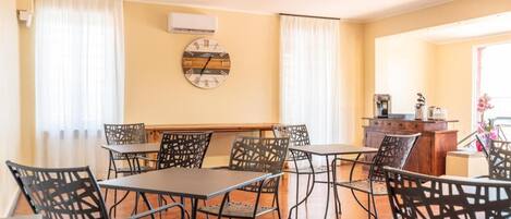 A dining area with a long table and chairs, a clock on the wall, and a window with curtains.
