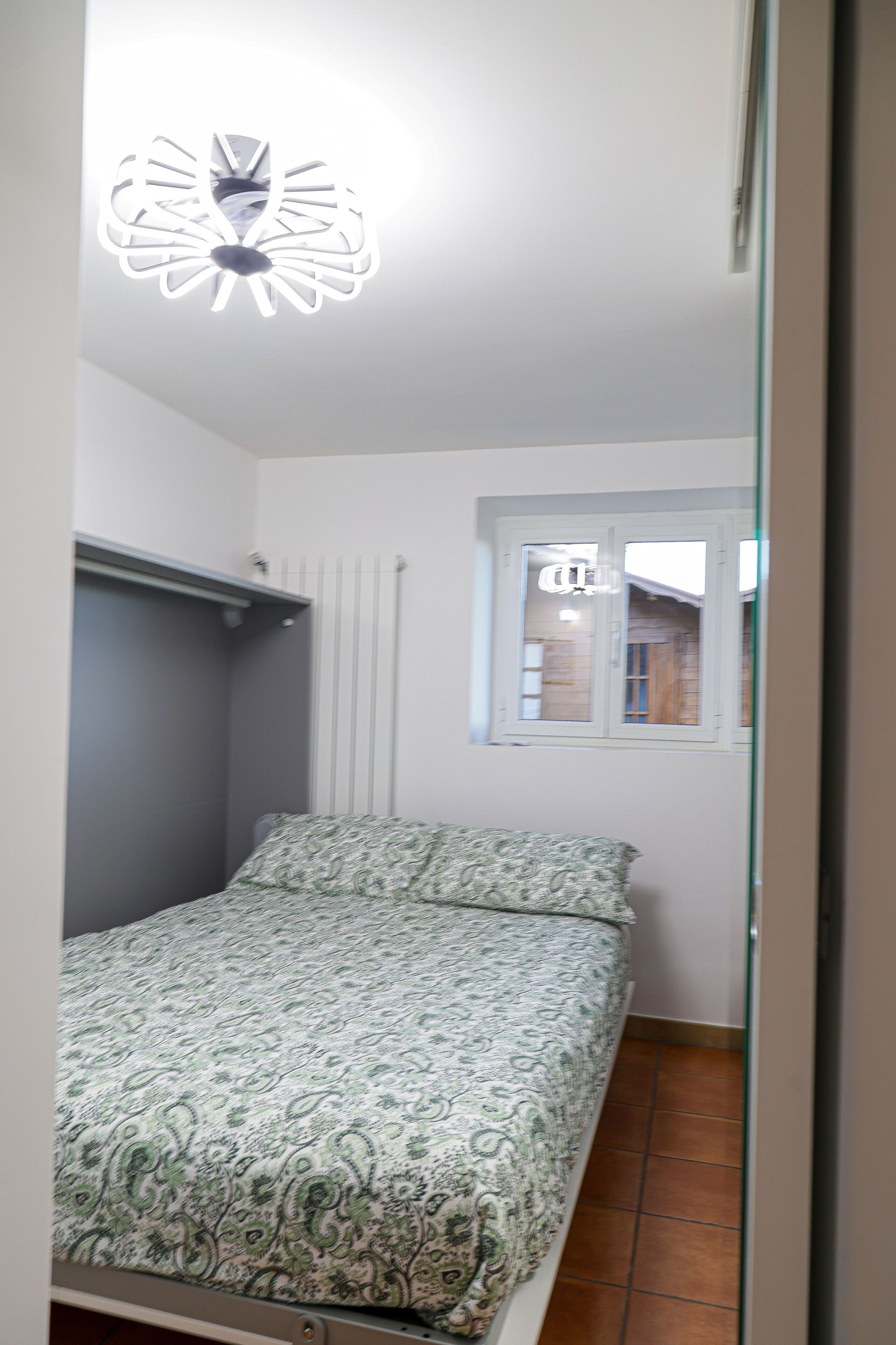 A bedroom with a bed, a window, and a ceiling light fixture.