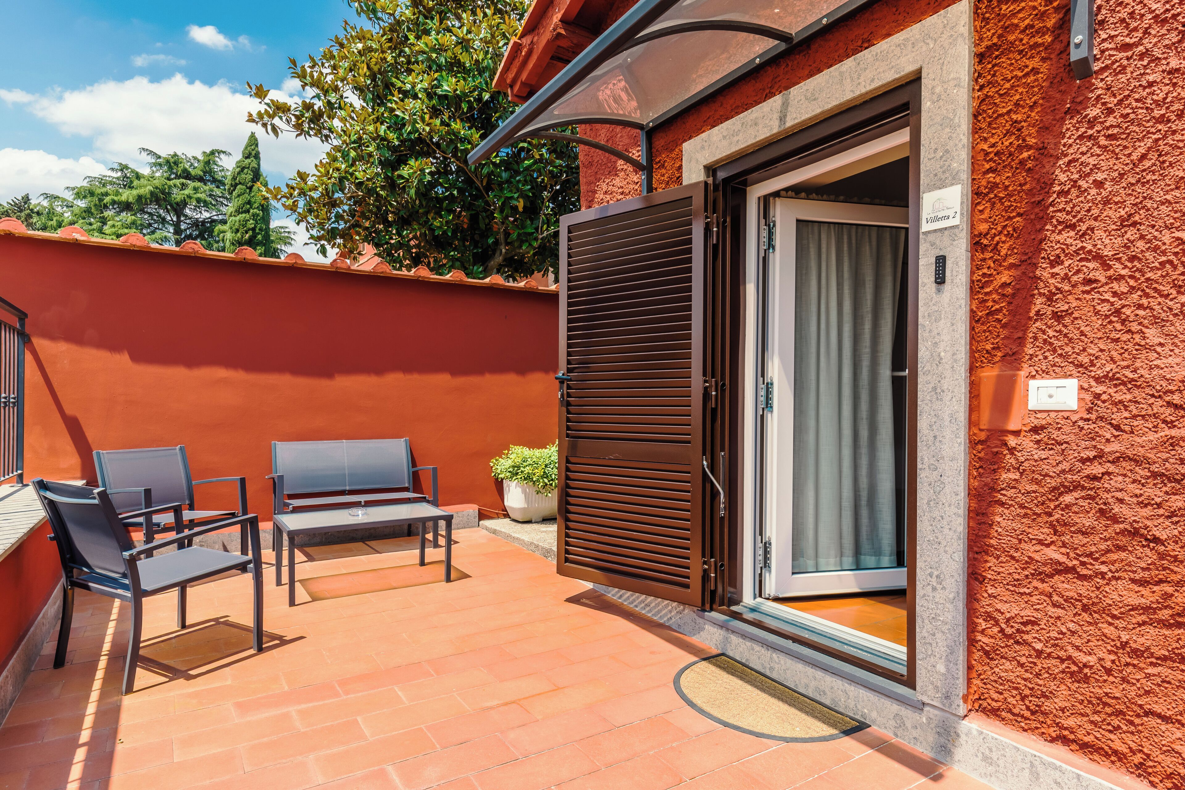 A patio with two chairs and a table, a sliding door to a room, and a potted plant.
