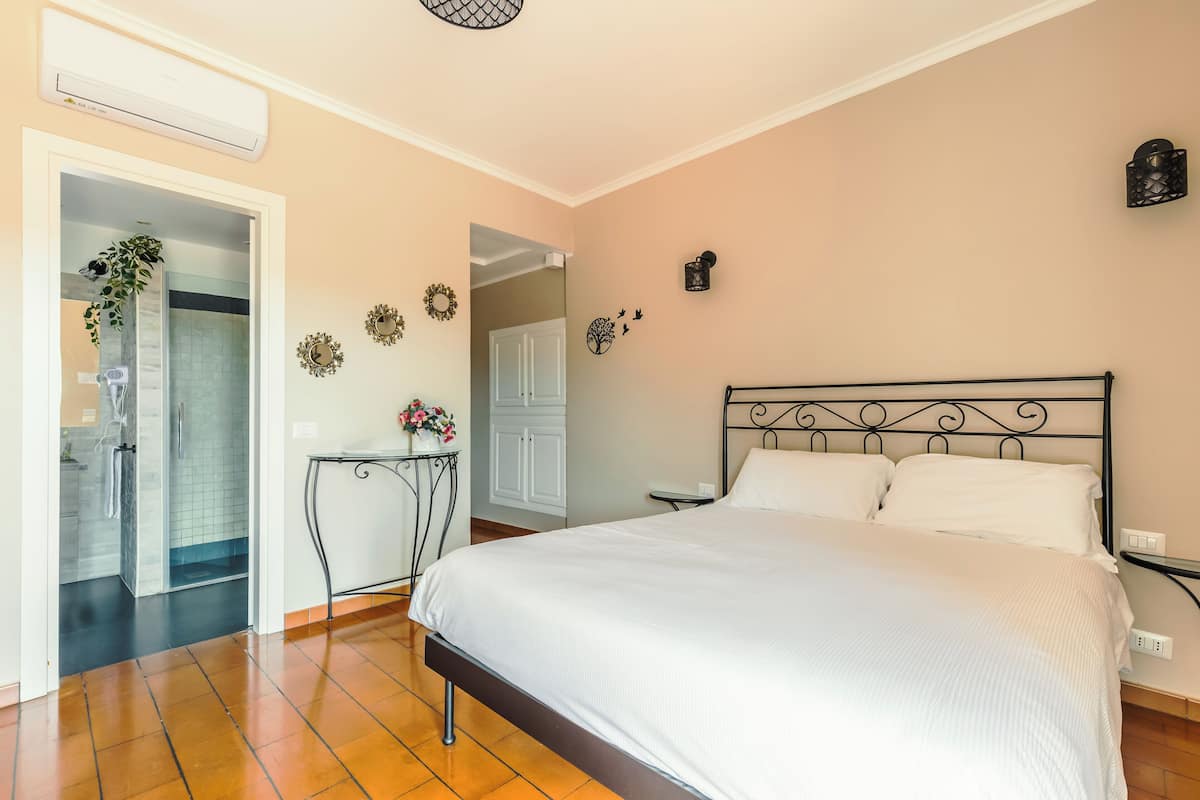 A bedroom with a large bed, a bedside table, a wall-mounted lamp, and a door leading to a bathroom.