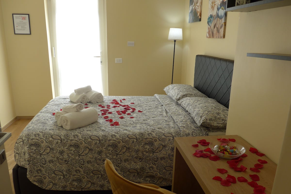 A hotel room with a bed, a bedside table with a bowl of fruit, and a chair.