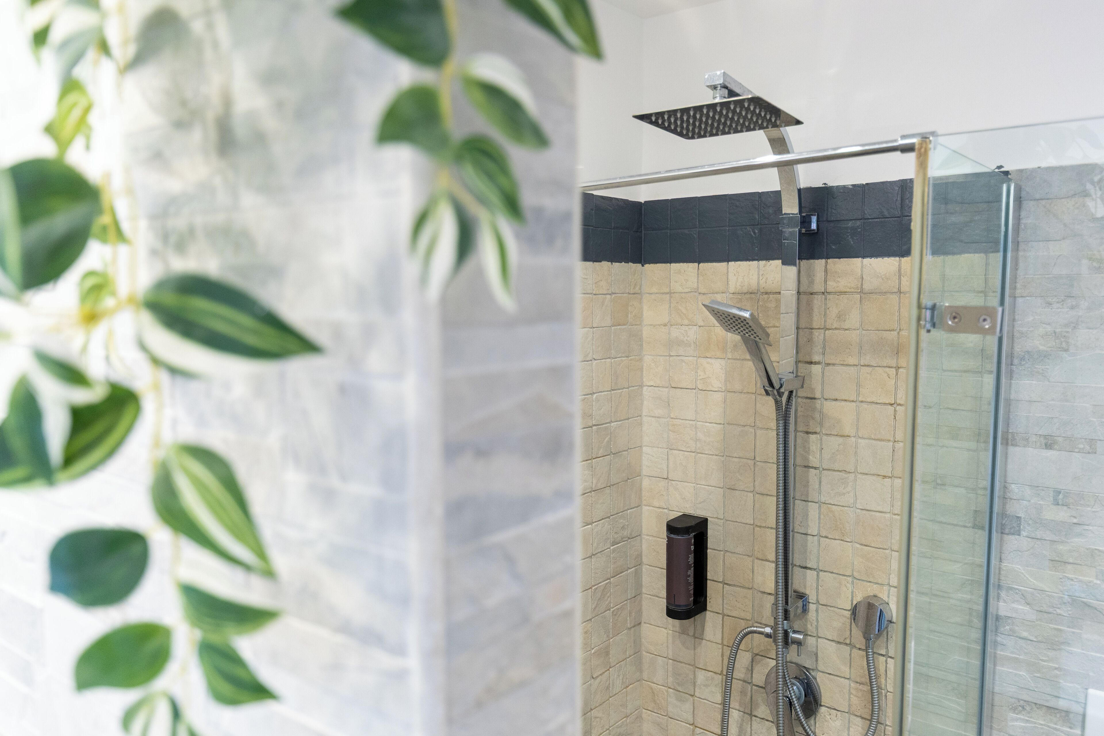 Une douche fermée par des parois en verre, dotée d’un pommeau de douche à main et d’un panneau de commande fixé au mur.