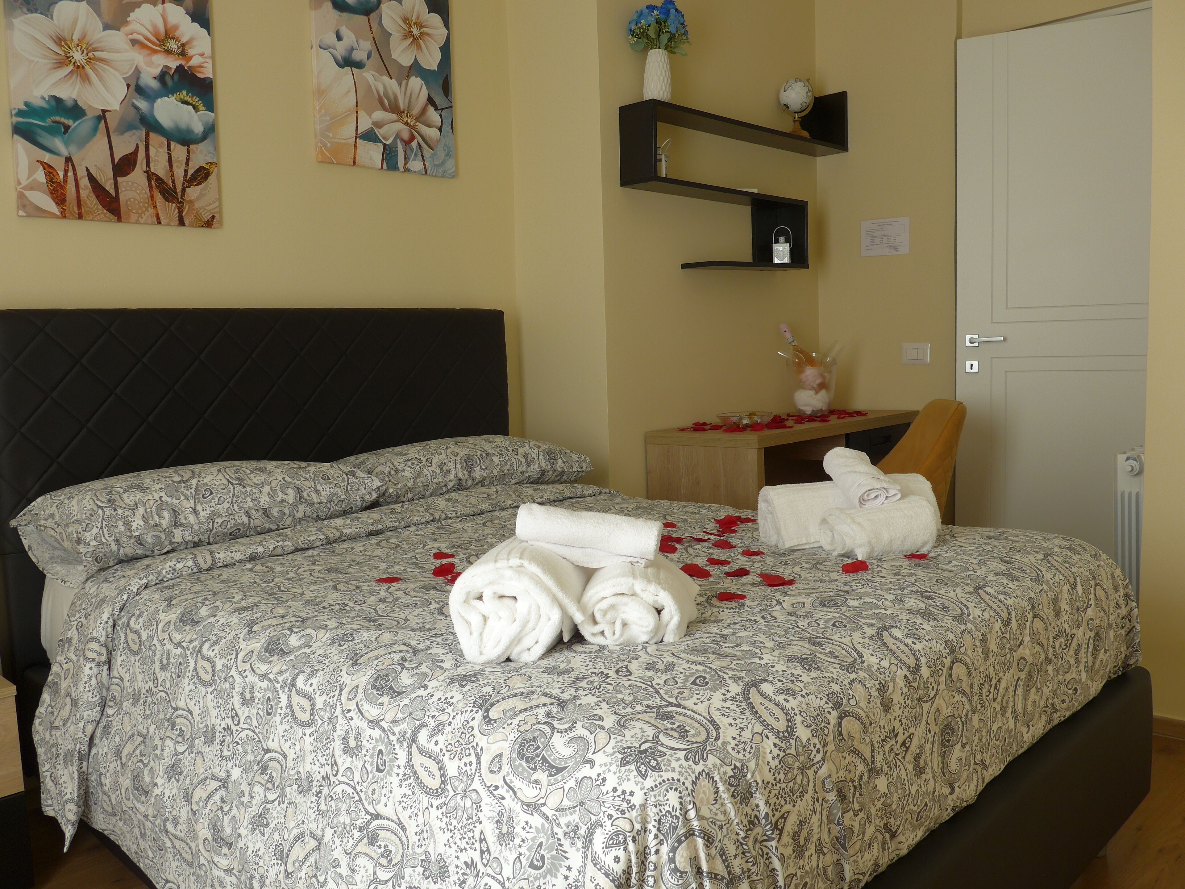 A hotel room with a large bed, a wooden nightstand, a globe, and a vase with flowers.