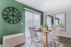 Un coin repas avec une table ronde, des chaises blanches et une grande horloge murale.