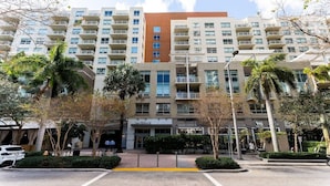 A multi-story hotel with a central courtyard, palm trees, and a storefront. - 1BR Miami Retreat w/BBQ, Pool, & Skyline Views (Miami)