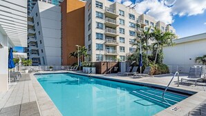 A swimming pool with lounge chairs and palm trees, surrounded by modern buildings. - 1BR Miami Retreat w/BBQ, Pool, & Skyline Views (Miami)