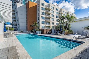 A swimming pool with lounge chairs and palm trees, surrounded by modern buildings. - 1BR Miami Retreat w/BBQ, Pool, & Skyline Views (Miami)