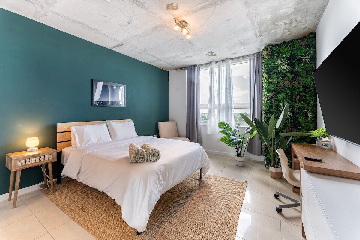 A modern bedroom with a bed, bedside table, lamp, and a large window with curtains.
