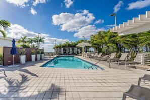 A swimming pool with lounge chairs and umbrellas, surrounded by palm trees and a clear sky.
