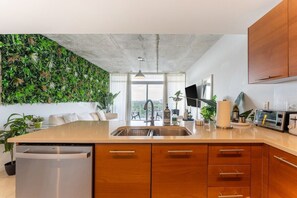 Une cuisine moderne avec un plafond en béton, des armoires en bois, un lave-vaisselle intégré et une grande fenêtre donnant sur un balcon.