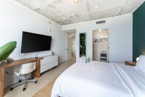 Une chambre moderne avec un grand lit, un bureau avec une chaise, un téléviseur à écran plat et un dressing.