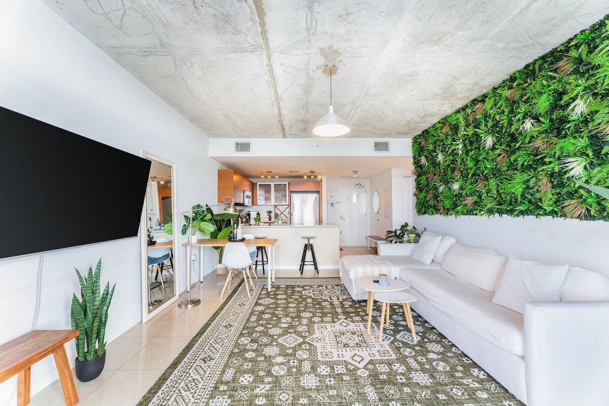 Een moderne woonkamer met een witte bank, een salontafel, een kamerkleed met een patroon en een groene wand met begroeiing.
