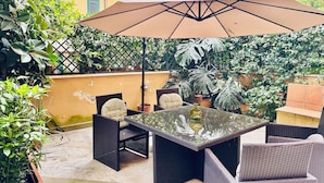 Eine Außenpatio mit Korbmöbeln, einem Glastisch und einem großen Sonnenschirm.