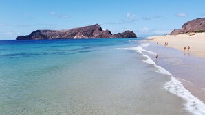Una playa con aguas turquesas cristalinas, una orilla arenosa y acantilados rocosos al fondo.