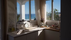 Una cocina con un ventanal grande, un lavamanos y una encimera con un juego de té y un cuenco de fruta.