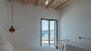 Un dormitorio con cama, una silla, un escritorio y vista al mar por una puerta corrediza.