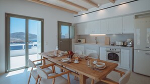Una cocina moderna con armarios blancos, una mesa de comedor de madera y vistas al mar a través de amplios ventanales.