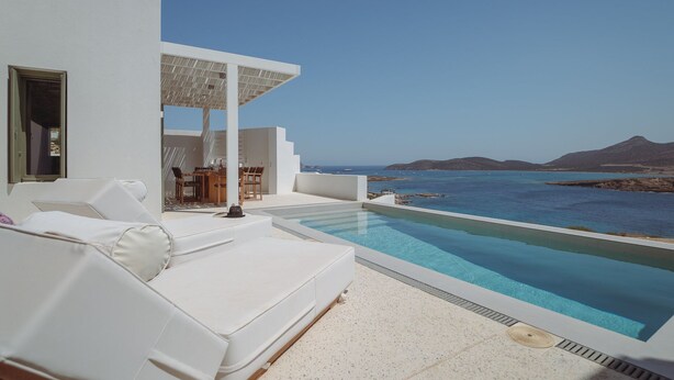 A modern outdoor pool area with a white infinity pool, white lounge chairs, and a table with chairs.