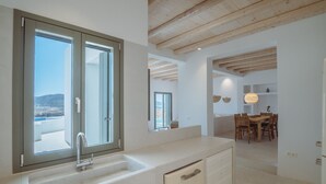 A modern kitchen with a large window, wooden ceiling beams, and a dining area with a table and chairs.