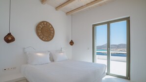 A bedroom with a large bed, a woven wall hanging, and a view of the sea through a sliding door.