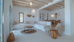 A spacious living area with a white sofa, a dining table, and a wooden ceiling.