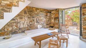 A stone-walled room with a white bench, wooden table, and chairs. - Stone Pine House | Antiparos (Soros)