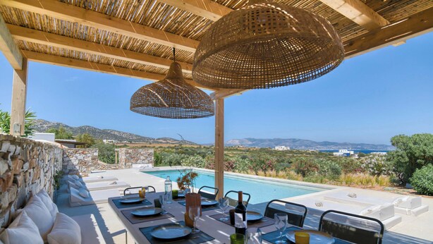 An outdoor dining area with a pool view, stone walls, and wicker overhead lighting. - Stone Pine House | Antiparos (Soros)