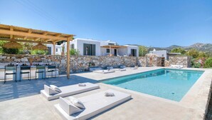 A modern outdoor pool area with lounge chairs and a pergola. - Stone Pine House | Antiparos (Soros)