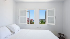 A bedroom with a bed, two windows, and a small table. - Orchard House | Antiparos (Agios Georgios)