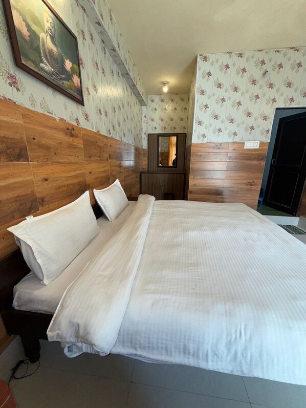Habitación de hotel con cabecera de madera, cama grande con ropa blanca y papel tapiz floral, además de un cuadro enmarcado de Buda.