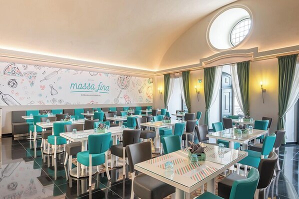 Ein Restaurant mit türkisfarbenen Stühlen und weißen Tischen, einer Wandmalerei mit Lebensmittelellustrationen und einem runden Oberlicht.