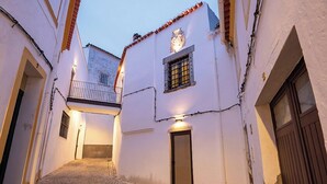 A narrow cobblestone street flanked by white buildings with tiled roofs, a balcony, and a door with a window. - Vila Gale Casas D'Elvas Historic Hotel (Elvas)