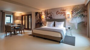 A hotel room with a large bed, a dining table with chairs, a small side table, and a wall mural. - Vila Gale Casas D'Elvas Historic Hotel (Elvas)