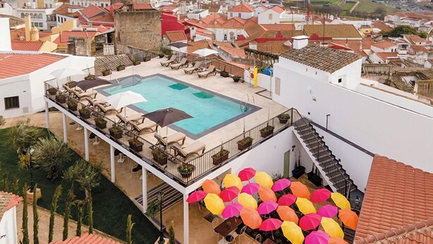 A rooftop pool area with lounge chairs and umbrellas, surrounded by buildings with red-tiled roofs. - Vila Gale Casas D'Elvas Historic Hotel (Elvas)