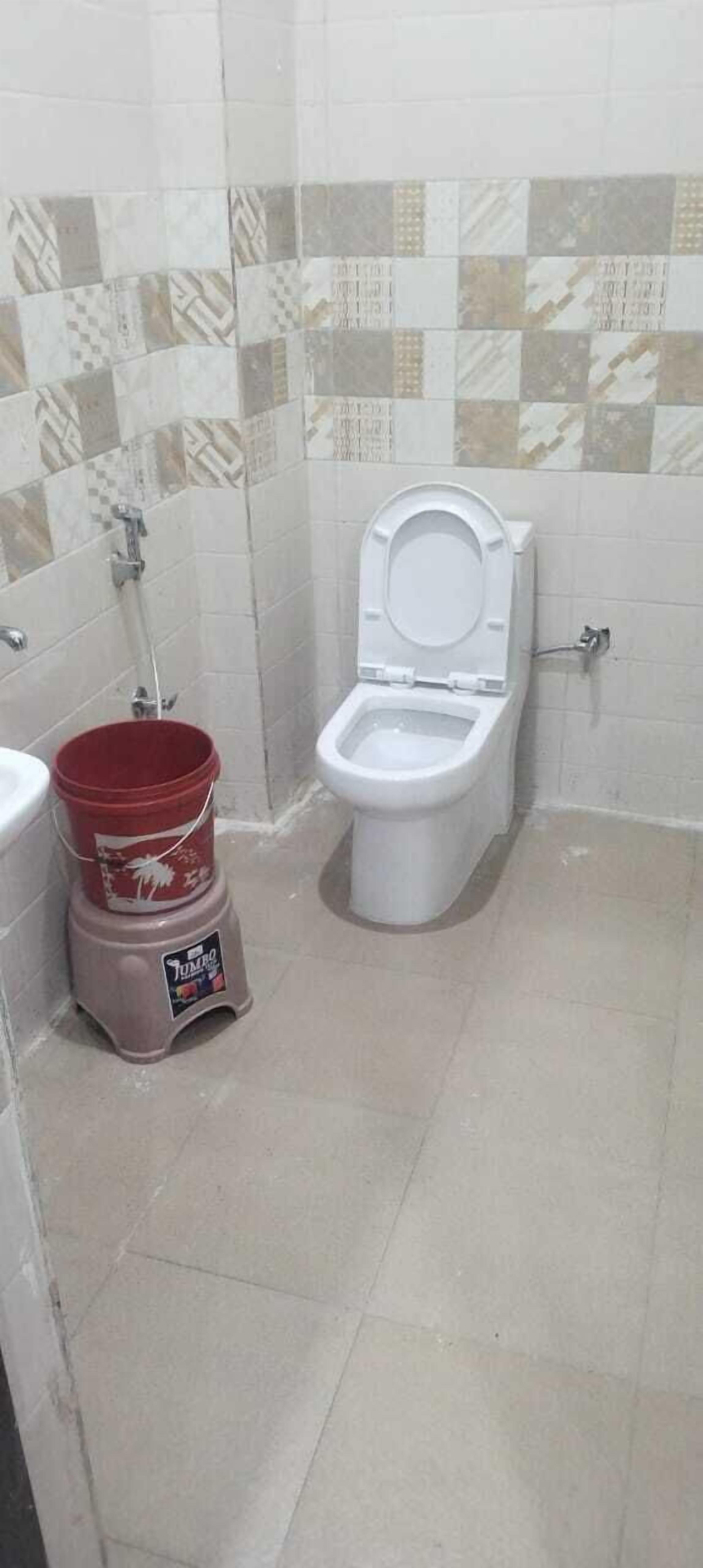 A bathroom with a toilet, a red bucket, and tiled walls.