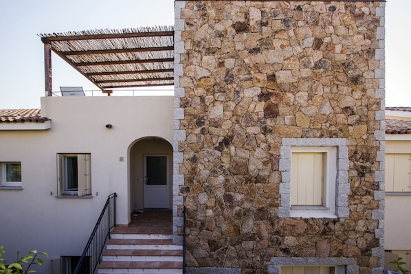 A building with a stone facade, a wooden pergola, and a staircase leading to an entrance.