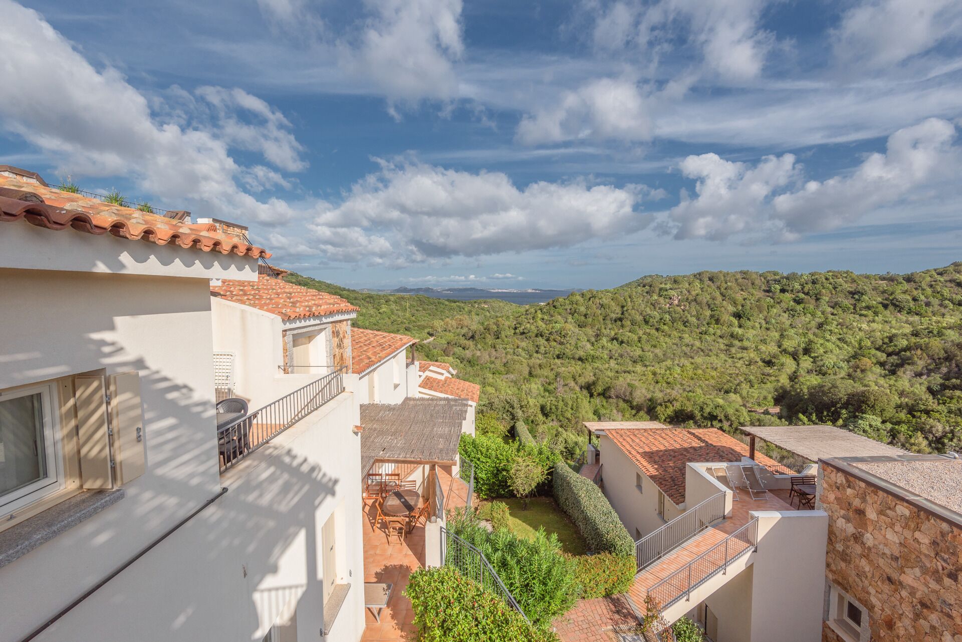 Un barrio residencial con techos de tejas de arcilla, paredes blancas y vistas a una ladera verde y exuberante.
