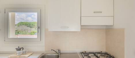 A kitchen with a window, a sink, a stove, and cabinets.