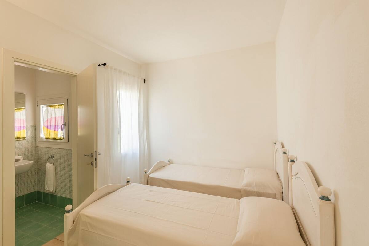 A bedroom with two beds, a bathroom with a sink and mirror, and a door leading to another room.