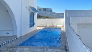 A swimming pool with stone tiles, white walls, and blue window grills. - Villa Dar Othman (cap zebib)