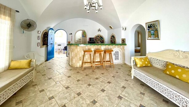 A spacious living area with a kitchen island, two sofas with cushions, a chandelier, and a fan. - Villa Dar Othman (cap zebib)