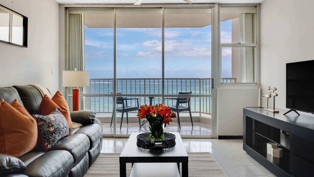 A modern living room with a balcony, a sofa, a coffee table with a vase of flowers, and a TV on a cabinet.