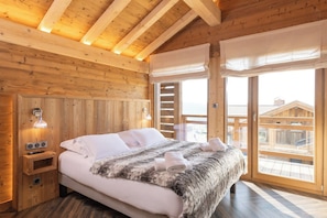 Ein Schlafzimmer einer Holzhütte mit einem Bett, Nachttischlampen und Blick durch ein großes Fenster.