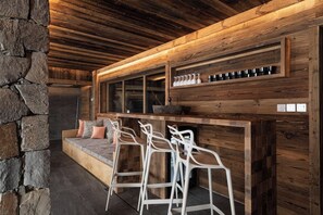Ein rustikaler Innenraum mit Steinwand, Holzbalkendecke und einer Bar mit Hockern.