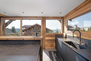 A modern kitchen with large windows, a built-in sink, and a wooden countertop.