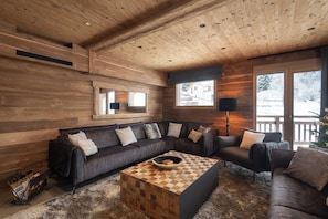 A cozy living room with a wooden ceiling, a sectional sofa, a coffee table, and a large window with a view. - ✨ La Vallée Cerena – Luxury Chalet with Indoor Pool, Sauna & Fireplace (Gérardmer)