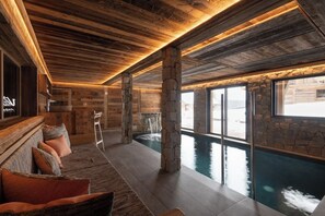 Ein Wellnessbereich mit Pool, Holzboden, Steinpfeilern und einer Sitzecke mit Kissen.