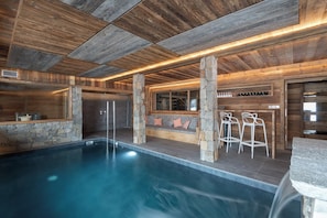 A modern indoor pool area with stone walls, wooden ceiling, and bar seating. - ✨ La Vallée Cerena – Luxury Chalet with Indoor Pool, Sauna & Fireplace (Gérardmer)