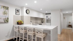 A modern kitchen with a white island, bar stools, a clock, and a framed picture on the wall.